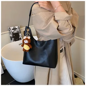 Detail of a large black hobo tote bag with a brown plush bear charm in a chic setting