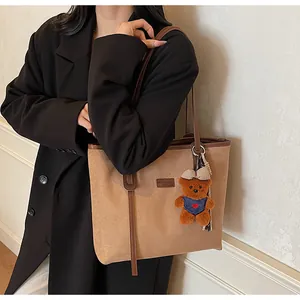 Detail einer khakifarbenen Wildleder-Shopper-Tasche mit braunen Tragegriffen und Bärenanhänger