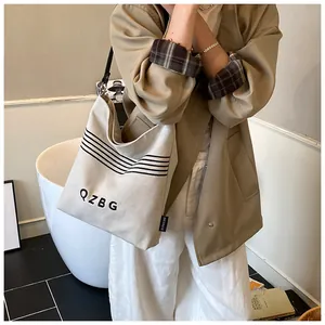 Close-up of beige canvas bucket bag featuring black QZBG lettering and stripes