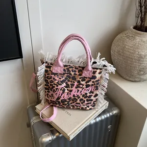Leopard print canvas tote bag with pink handles and fringes shown on a silver suitcase