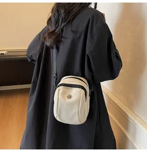 Detail of beige waterproof oxford cloth crossbody bag with black contrast zippers