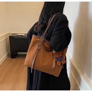 Braune Shopper-Tasche aus Wildleder mit Bärenanhänger getragen von einem Modell im Raum