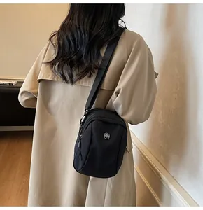 Practical black waterproof nylon crossbody bag shown with a stylish khaki trench coat