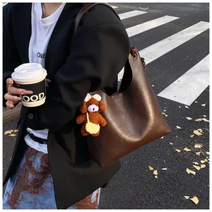 Detail of dark brown tote bag with glossy leather texture and cute plush bear charm