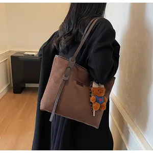 Braune Wildleder-Tragetasche mit Bärenanhänger über der Schulter auf schwarzem Blazer