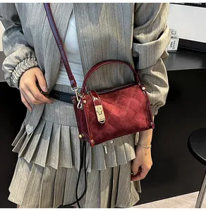 Detail view of burgundy quilted crossbody bag with gold hardware on a model with grey suit