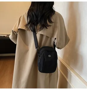 Detail of a black nylon crossbody bag worn over a beige trench coat for a casual look