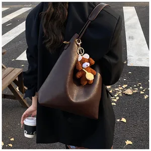 Detail of dark brown leather tote bag with plush bear charm in autumn street scene