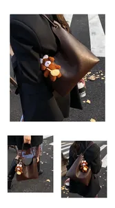 Detail of dark brown tote bag with glossy leather texture and a cute teddy bear charm