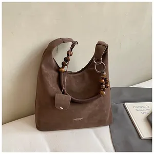 Detail of dark brown suede tote featuring wooden beads and metal ring on the strap