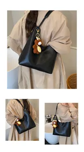 Detail of black pebbled leather tote bag featuring a cute brown plush bear charm