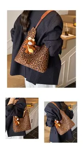 Detail view of leopard print tote bag with brown leather strap and plush bear charm