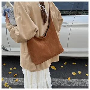 Close-up of brown matte suede hobo bag carried by hand in a crisp autumn street setting