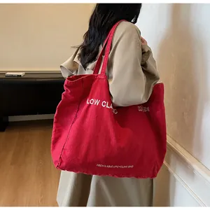 Vue détaillée du sac cabas en toile rouge avec logo blanc sur l'épaule d'un mannequin