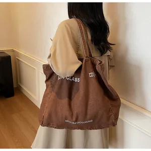 Gros plan d'un sac fourre-tout en toile marron avec broderie porté sur un trench-coat
