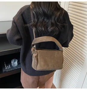 Detail of a dark brown suede shoulder bag with pleated side and silver metal hook