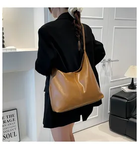 Close-up of a large tan PU leather tote bag worn by a model in a modern indoor setting