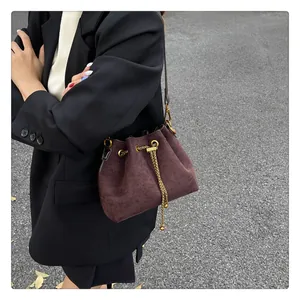 Detail of dark brown suede bucket bag with gold chain drawstring on a black blazer