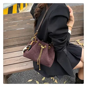 Detail of dark coffee drawstring bucket bag with gold chain and beaded pendant