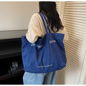 Détail d'un grand cabas en jean bleu foncé avec texte blanc porté par un mannequin
