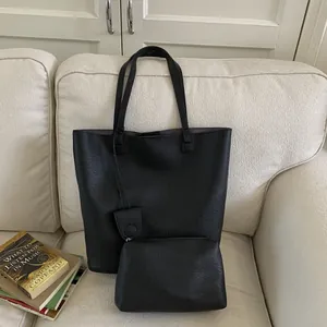 Detail of black pebbled leather tote bag with matching zippered pouch on sofa