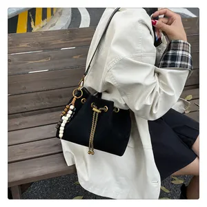 Detail of black drawstring bucket bag featuring gold chain and beaded charm accessory