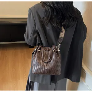 Detail of woven brown bucket bag featuring a geometric strap on a female model
