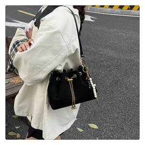 Detail of minimalist black drawstring bucket bag with gold chain and beaded charm
