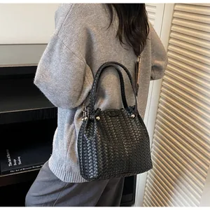 Close-up of black woven bucket bag with silver rivet details and textile shoulder strap