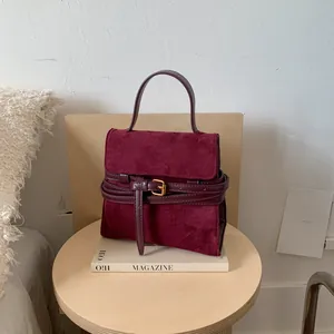 Retro burgundy suede handbag with elegant gold buckle on a minimalist wooden stool