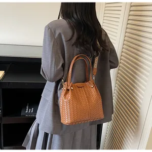 Detail of a brown woven leather bucket bag with gold hardware and wide shoulder strap