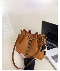 Detailed view of brown suede bucket bag with chain drawstring and beaded accent on a desk