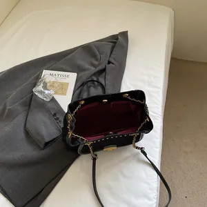 Elegant black leather tote bag with gold studs and chain strap on white linen