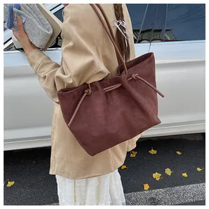 Detail of burgundy suede tote bag featuring drawstring knots in an autumn street setting