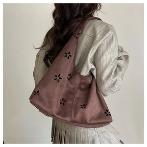 Detail of laser-cut flower patterns on a brown faux suede tote bag worn by a model