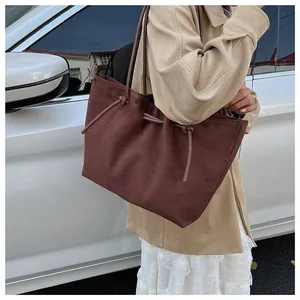Brown suede tote bag with drawstring detail shown as a shoulder bag in street style