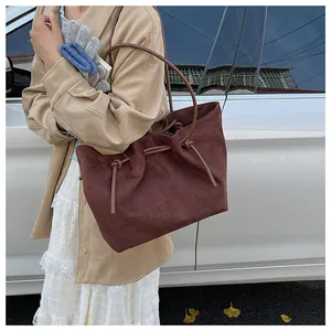 Detail of a dark brown suede tote bag featuring slim leather straps and drawstring accents