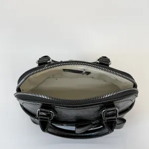 Minimalist black shell bag with shiny leather texture and bow detail on light background