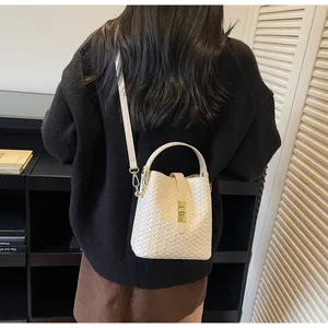 Shoulder view of a white woven bucket bag with gold twist lock and adjustable strap