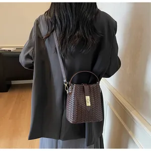 Detailed view of dark brown woven bucket bag with metal clasp worn by a model