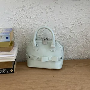 Minimalist mint green shell handbag with bow detail on a rustic wooden desk