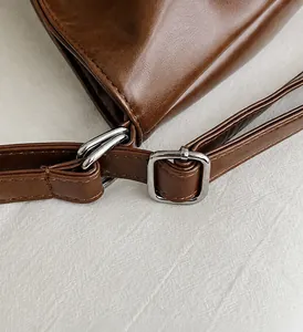 Detailansicht der silbernen Hardware-Verstellschnalle am braunen Leder-Schultergurt
