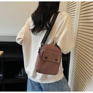 Close-up of a brown nylon crossbody bag with double black buttons and a wide strap