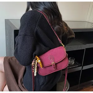 Close-up of wine red suede crossbody bag with colorful bead charm on shoulder strap