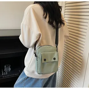 Detail of light green canvas crossbody bag with front flap pocket and black strap