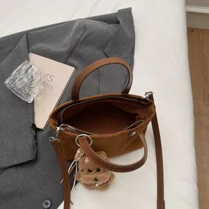 Brown suede mini square handbag with teddy dog charm on a cozy white bed setting