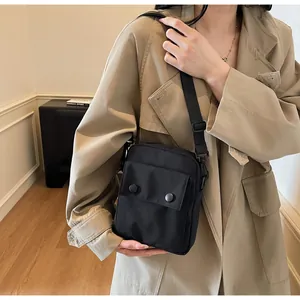 Close-up of black canvas crossbody bag with metal snap buttons on beige trench coat
