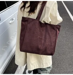 Detail shot of a large burgundy matte leather tote bag worn by a model in a trench coat