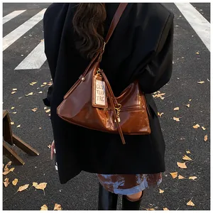 Detail of a brown patent leather tote bag with metallic zipper on a city street background