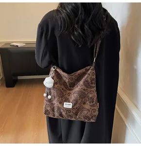 Detail of a brown paisley shoulder bag with a white plush cloud charm and logo patch